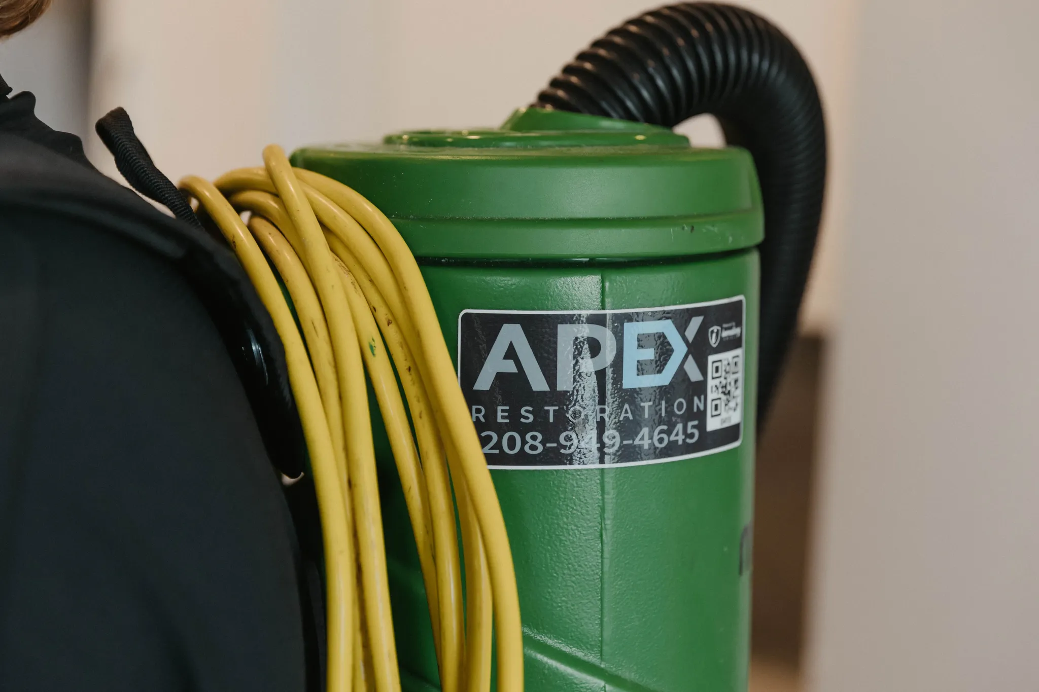 Apex Restoration technician in branded uniform removing mold from a water-damaged wall during indoor remediation work.